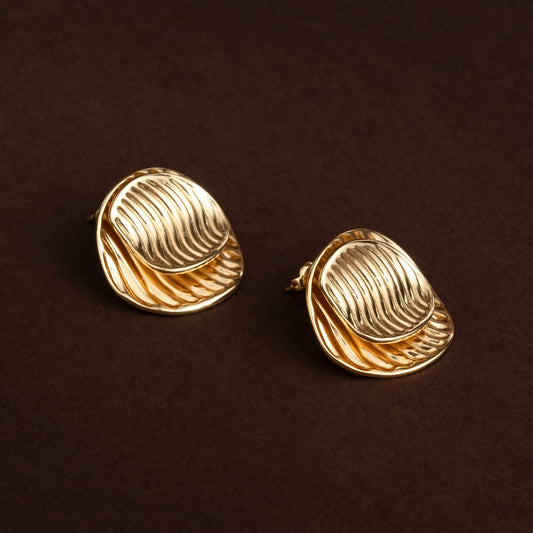 Brincos de botão dourados com formato orgânico e textura de linhas onduladas em relevo (design aura) em aço inoxidável sobre fundo escuro.