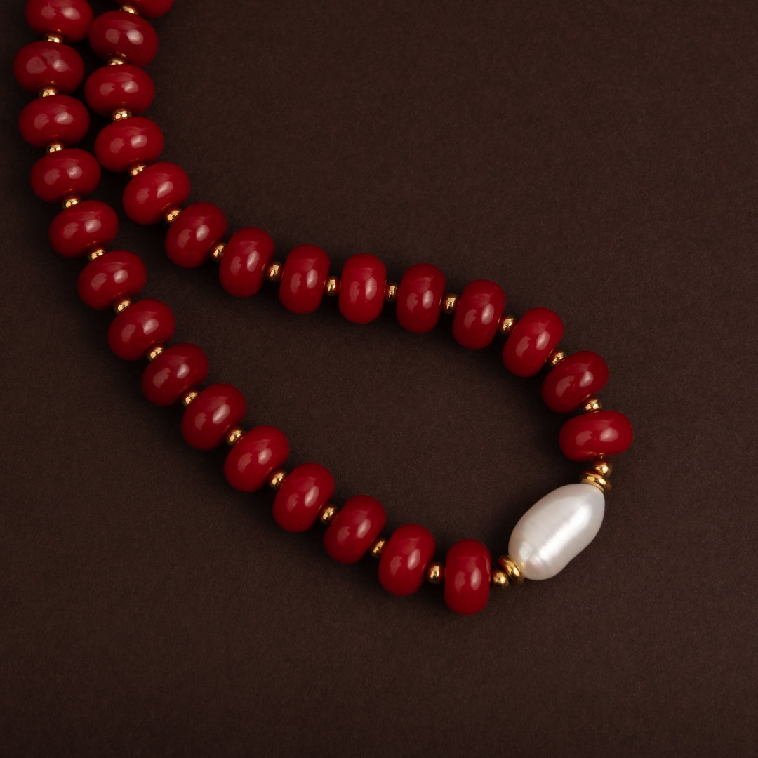 Detalhe macro das contas vermelhas brilhantes e da pérola barroca central do colar Vénus
