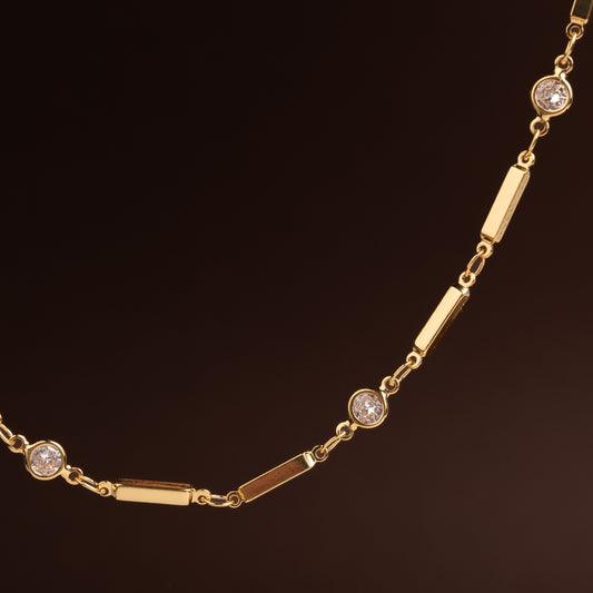 Colar de corrente dourada com elos ovais médios entrelaçados e fecho frontal redondo em aço inoxidável sobre fundo escuro.