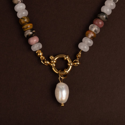 Detalhe do fecho boia dourado com pendente de pérola barroca branca num colar de contas de pedras naturais em tons de castanho, cinza e rosa.