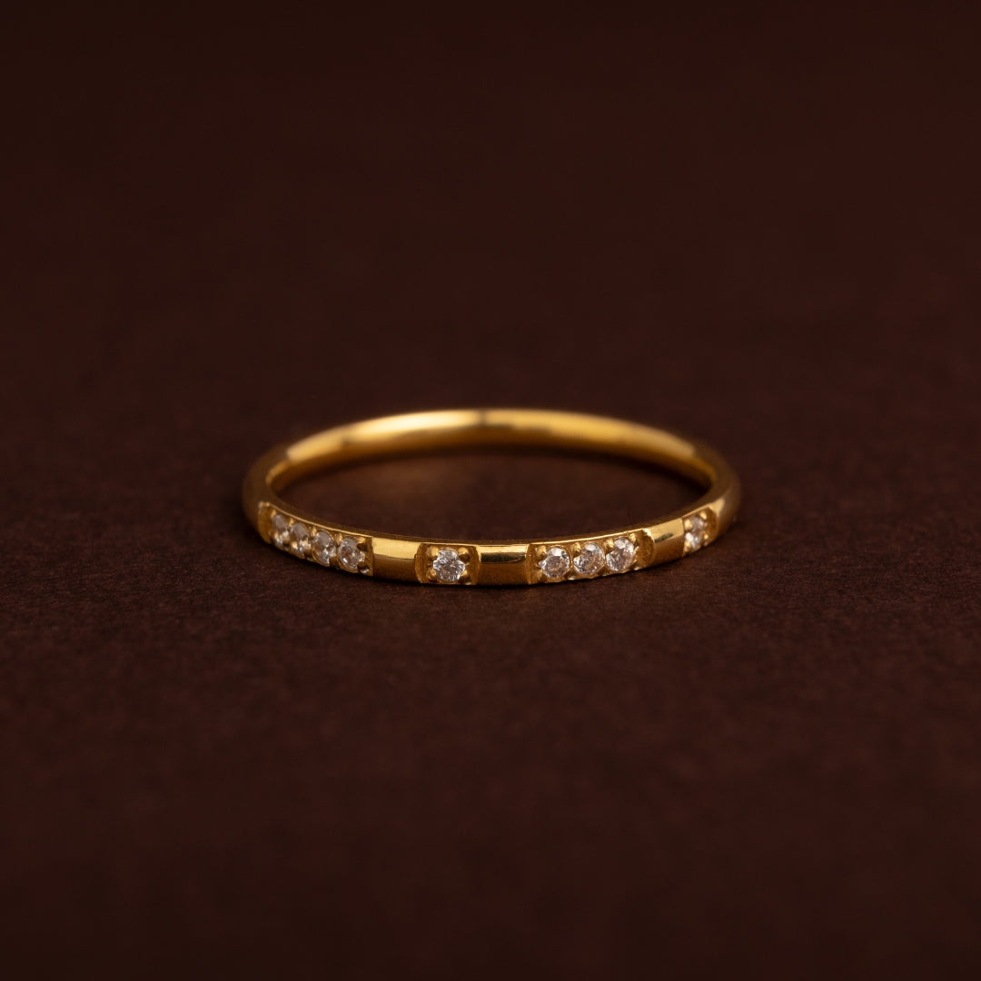 Anel fino dourado em aço inoxidável com padrão alternado de segmentos lisos e pequenos cristais cravados, estilo meia aliança.