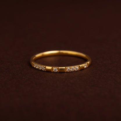 Anel fino dourado em aço inoxidável com padrão alternado de segmentos lisos e pequenos cristais cravados, estilo meia aliança.