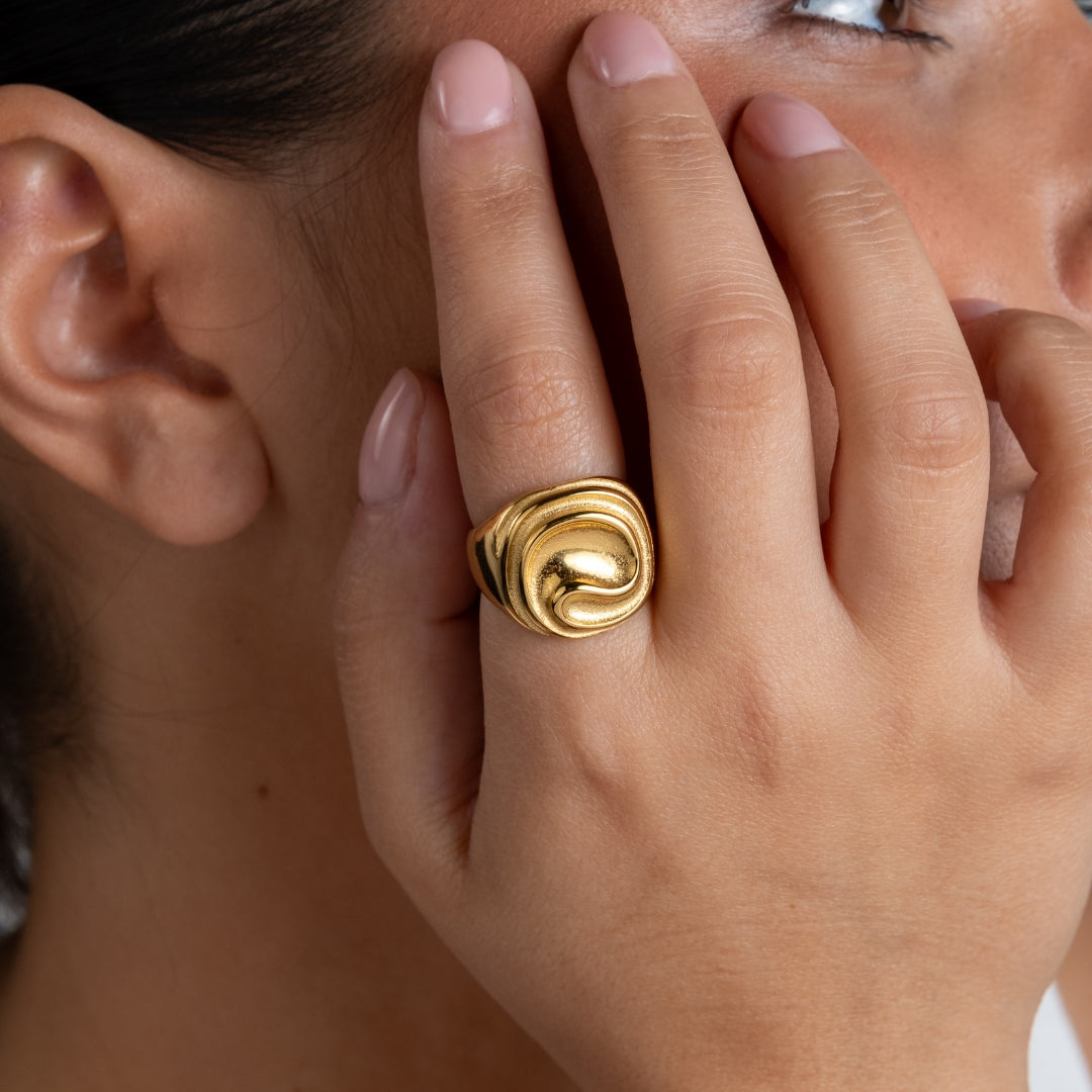 Anel Trace sinete em aço inoxidável dourado e prateado com relevo ondulado design contemporâneo coleção Fuse.
