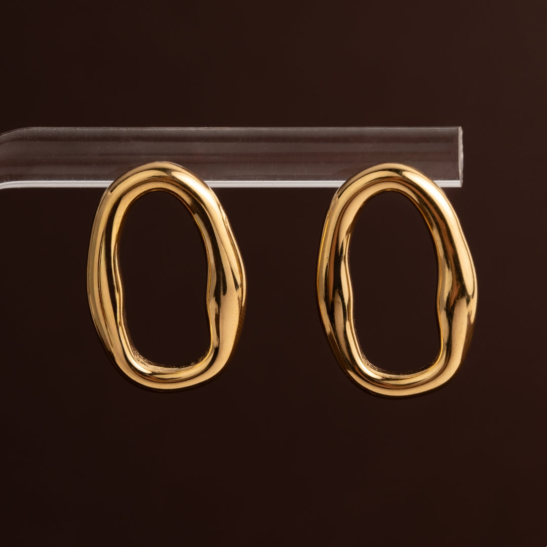Brincos de aço inoxidável dourado com formato de elo oval aberto, irregular e orgânico, com acabamento polido brilhante.