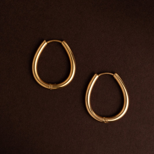 Par de argolas médias de formato oval ou em U, em aço inoxidável dourado com acabamento polido e liso sobre fundo escuro.