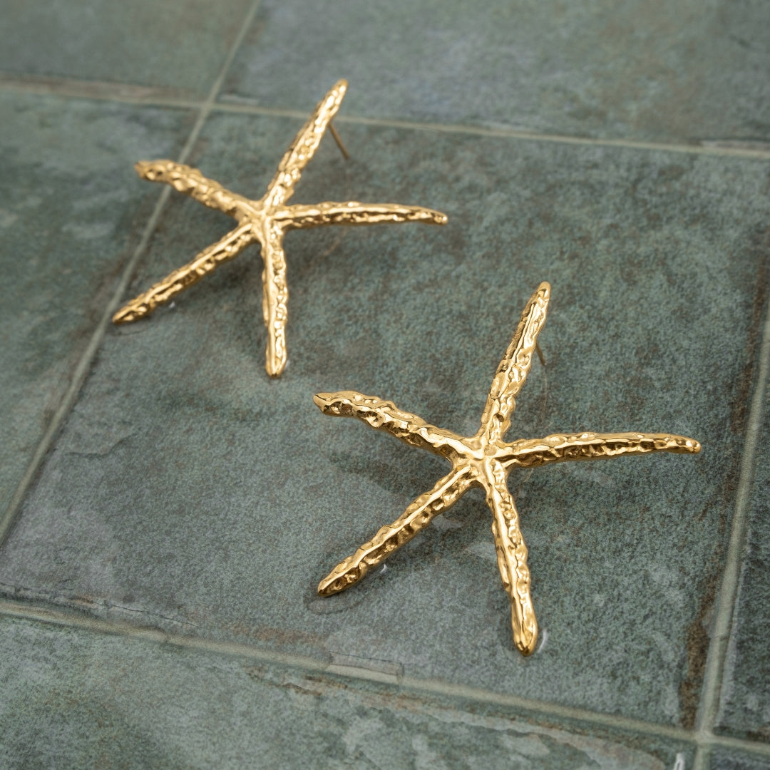Par de Brincos Estrela do Mar dourados grandes em aço inoxidável sobre azulejo verde-escuro