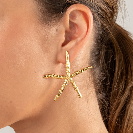 Modelo de perfil a usar os Brincos Estrela do Mar maxi em aço inoxidável dourado com textura orgânica.