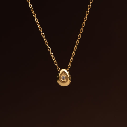 Colar fino dourado em aço inoxidável com pendente pequeno em forma de gota de metal maciço com um cristal brilhante no centro.
