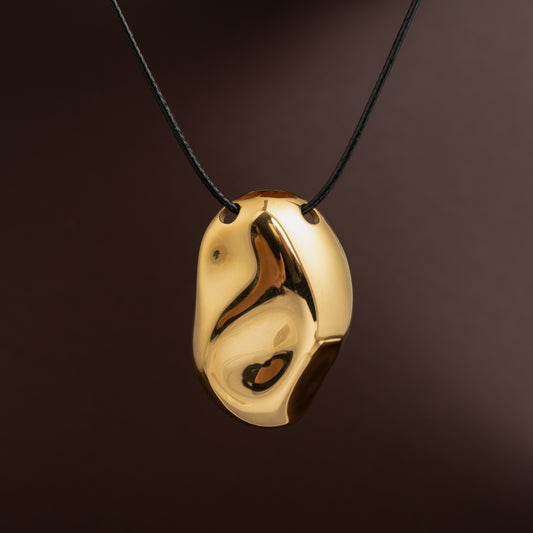 Pendente dourado grande com formato orgânico irregular e superfície polida suspenso num fio preto simples.