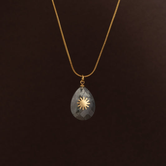 Detalhe do pendente talismã mostrando a pedra cinza facetada translúcida e o símbolo solar em relevo.