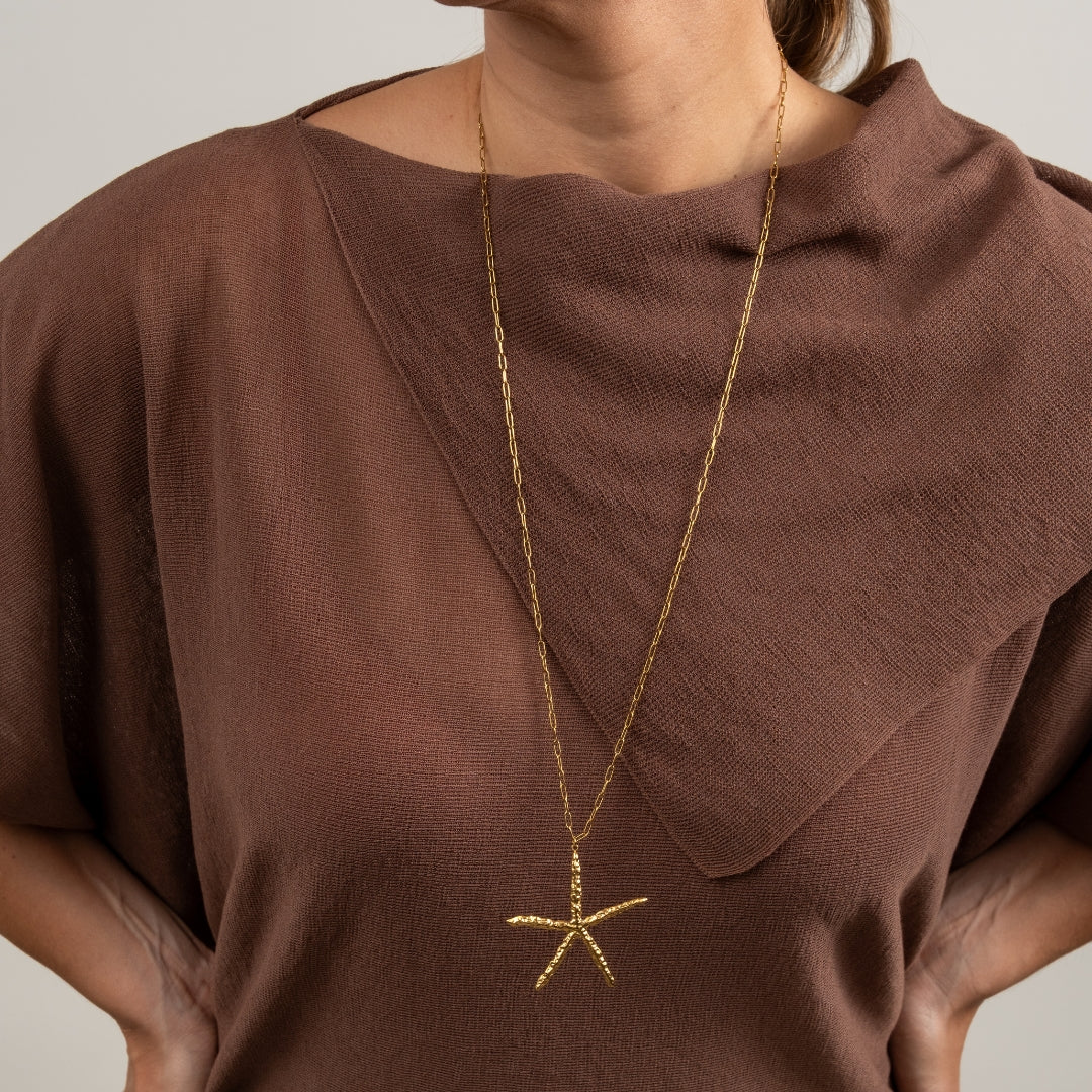 Modelo a usar o Colar Estrela do Mar dourado de forma comprida sobre uma camisola castanha