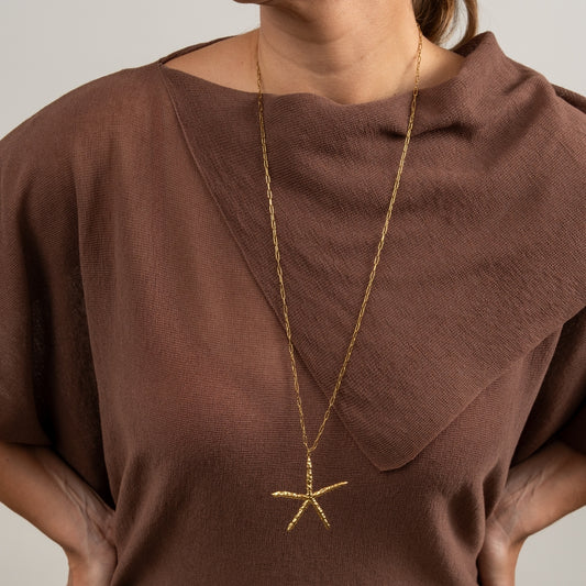 Modelo a usar o Colar Estrela do Mar dourado de forma comprida sobre uma camisola castanha
