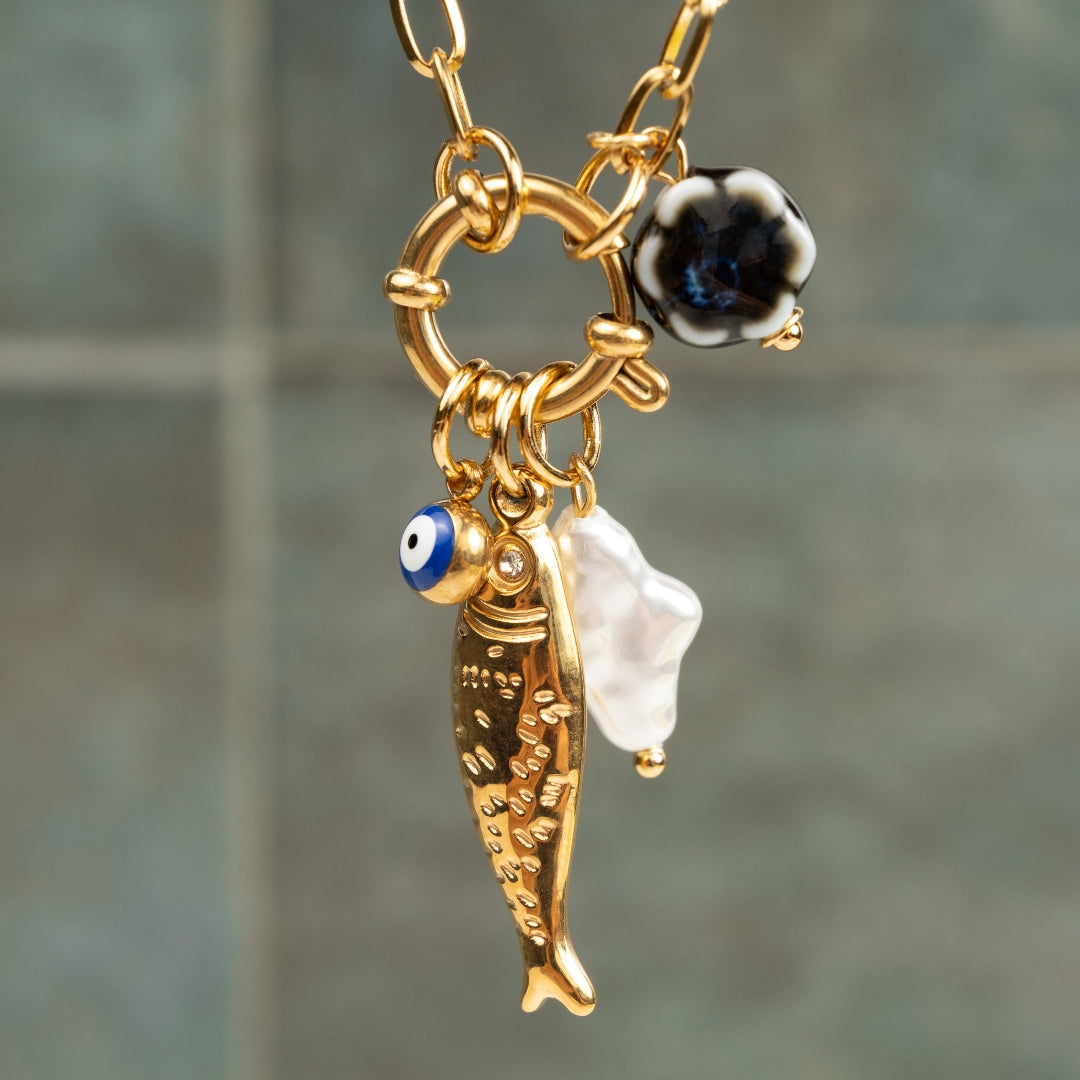 Detalhe em grande plano do Colar Costa Nova com pendente de peixe dourado, olho turco azul e pérola barroca