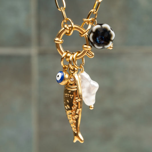Detalhe em grande plano do Colar Costa Nova com pendente de peixe dourado, olho turco azul e pérola barroca