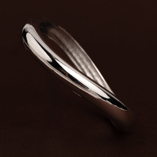 Pulseira rígida prateada estilo bangle com forma orgânica torcida e polimento espelhado.